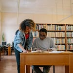Two university students studying together in a library, focusing on textbooks and learning.