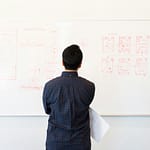 Man analyzing design flowchart on whiteboard in a professional office setting.
