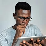 Young man wearing glasses engrossed in using a tablet device indoors.