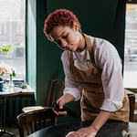 Young waitress cleans a table in a cozy café, capturing the essence of service and hospitality.