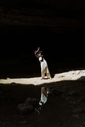 Black woman posing gracefully in a sunlit cavern creating a dramatic reflection.
