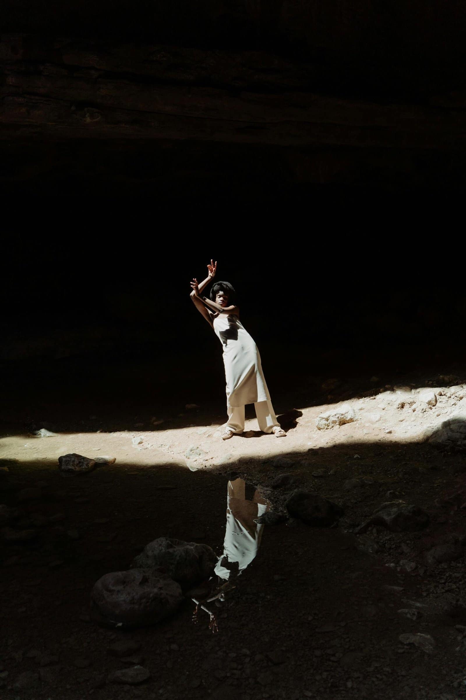 Black woman posing gracefully in a sunlit cavern creating a dramatic reflection.