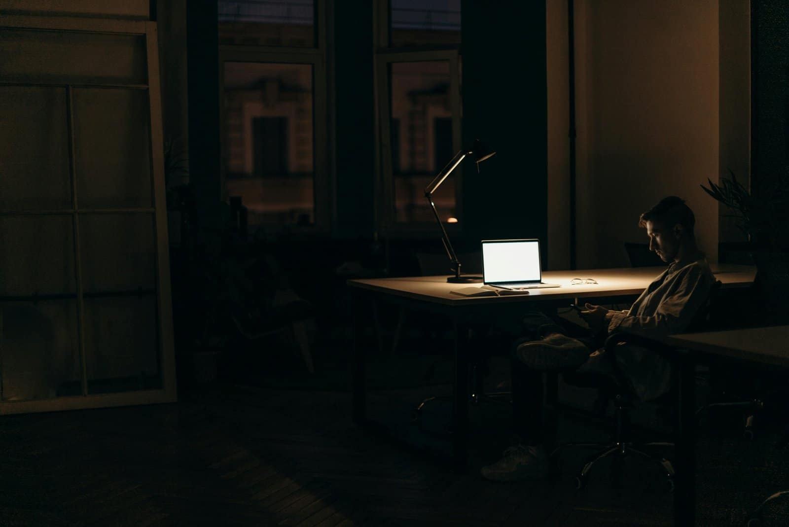 A man working late at night in a dimly lit office, with a bright laptop screen.