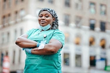 Proud nurse with arms crossed, in uniform, outdoors, urban setting, showing confidence and professionalism.