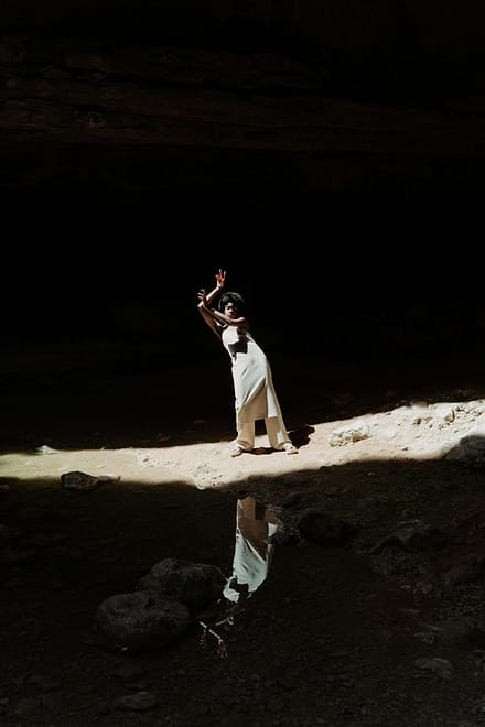 Black woman posing gracefully in a sunlit cavern creating a dramatic reflection.